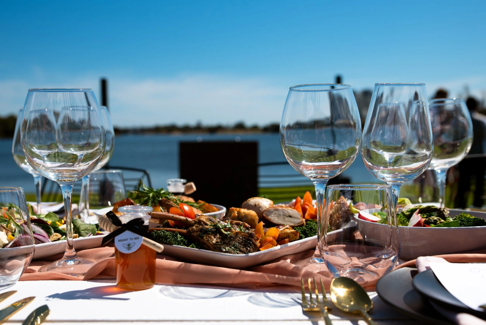 Food and glassware set out beside the water in natural daylight
